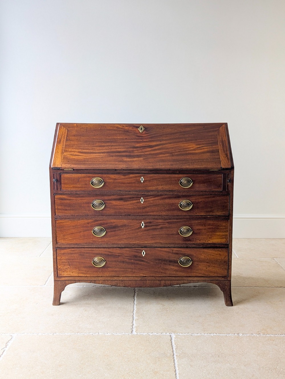 An antique Georgian mahogany slant-front bureau featuring four graduated long drawers with brass oval drop handles and shaped bracket feet. View III