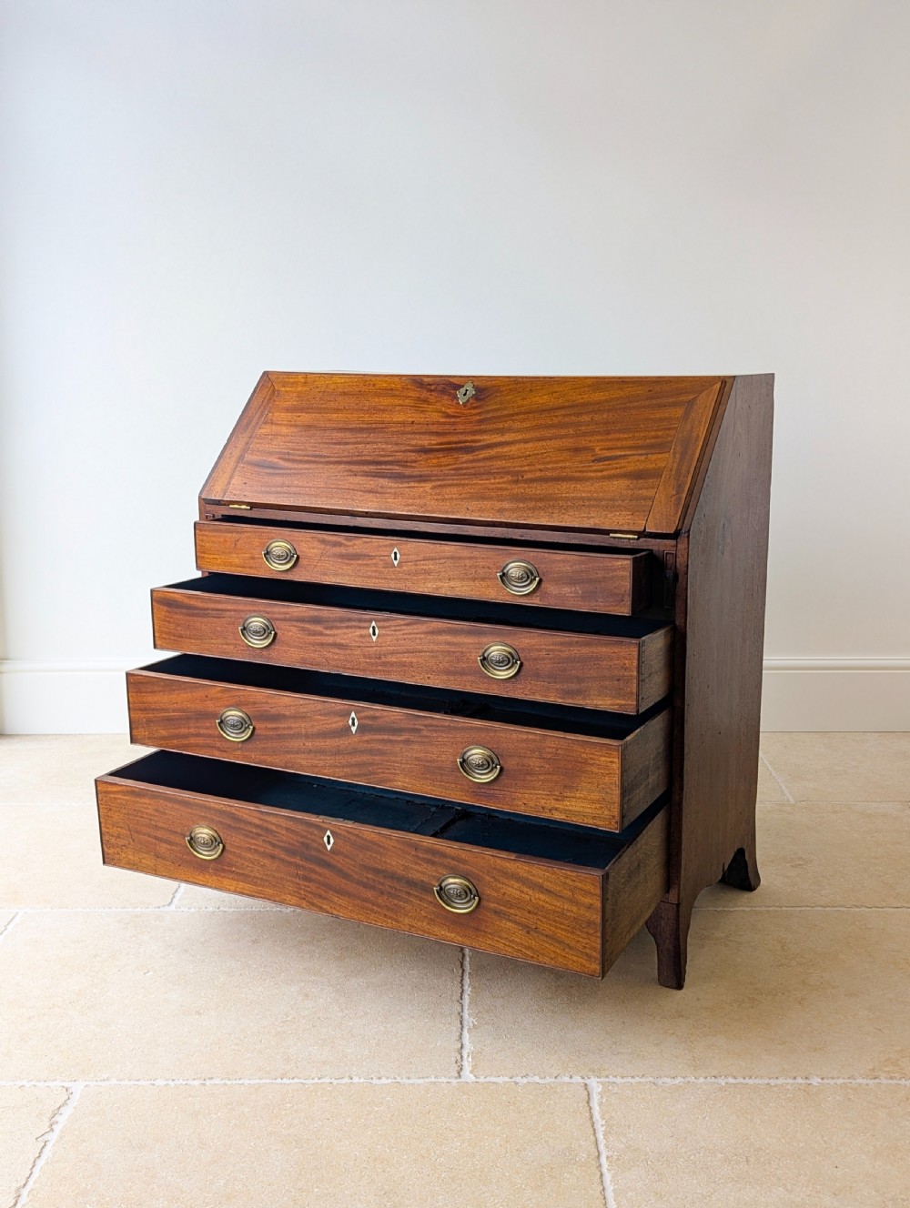 An antique Georgian mahogany slant-front bureau featuring four graduated long drawers with brass oval drop handles and shaped bracket feet. View IV