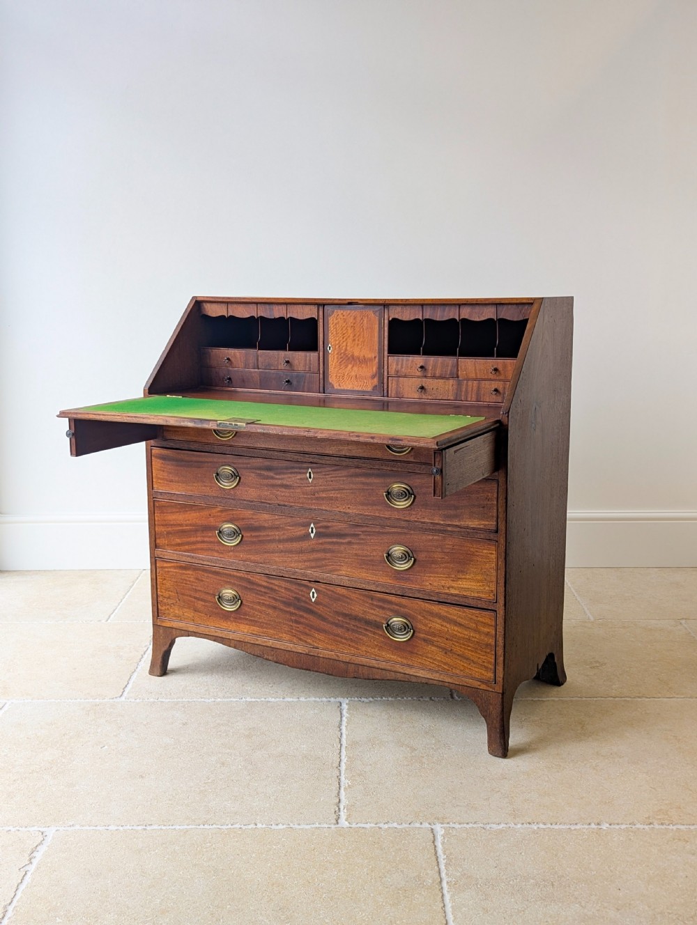 An antique Georgian mahogany slant-front bureau featuring four graduated long drawers with brass oval drop handles and shaped bracket feet. View VI