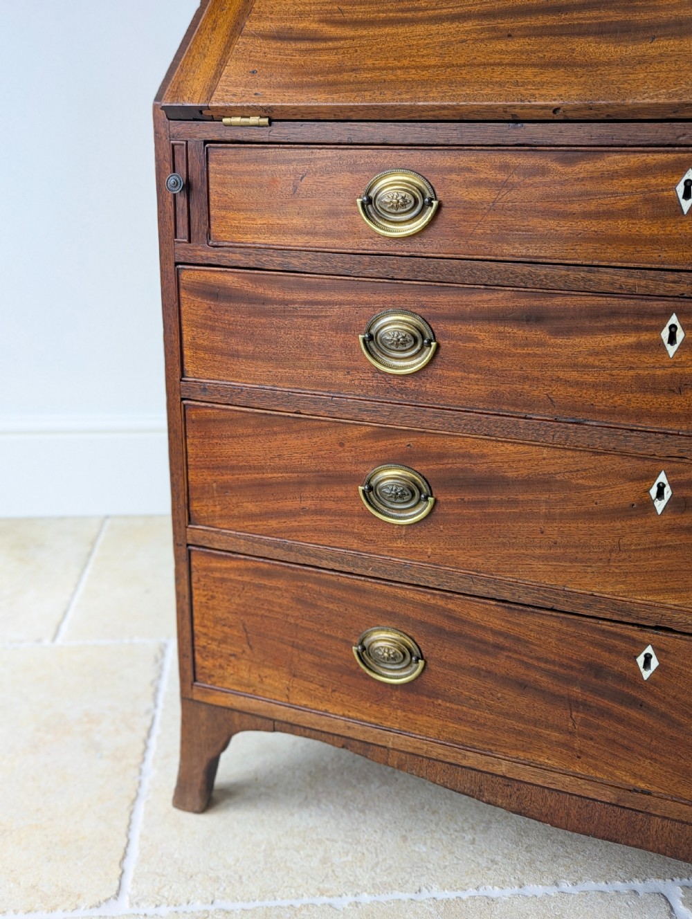An antique Georgian mahogany slant-front bureau featuring four graduated long drawers with brass oval drop handles and shaped bracket feet. View VII