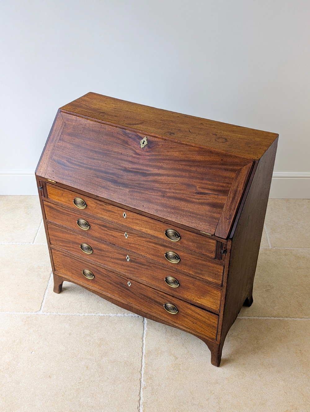 An antique Georgian mahogany slant-front bureau featuring four graduated long drawers with brass oval drop handles and shaped bracket feet. View VIII