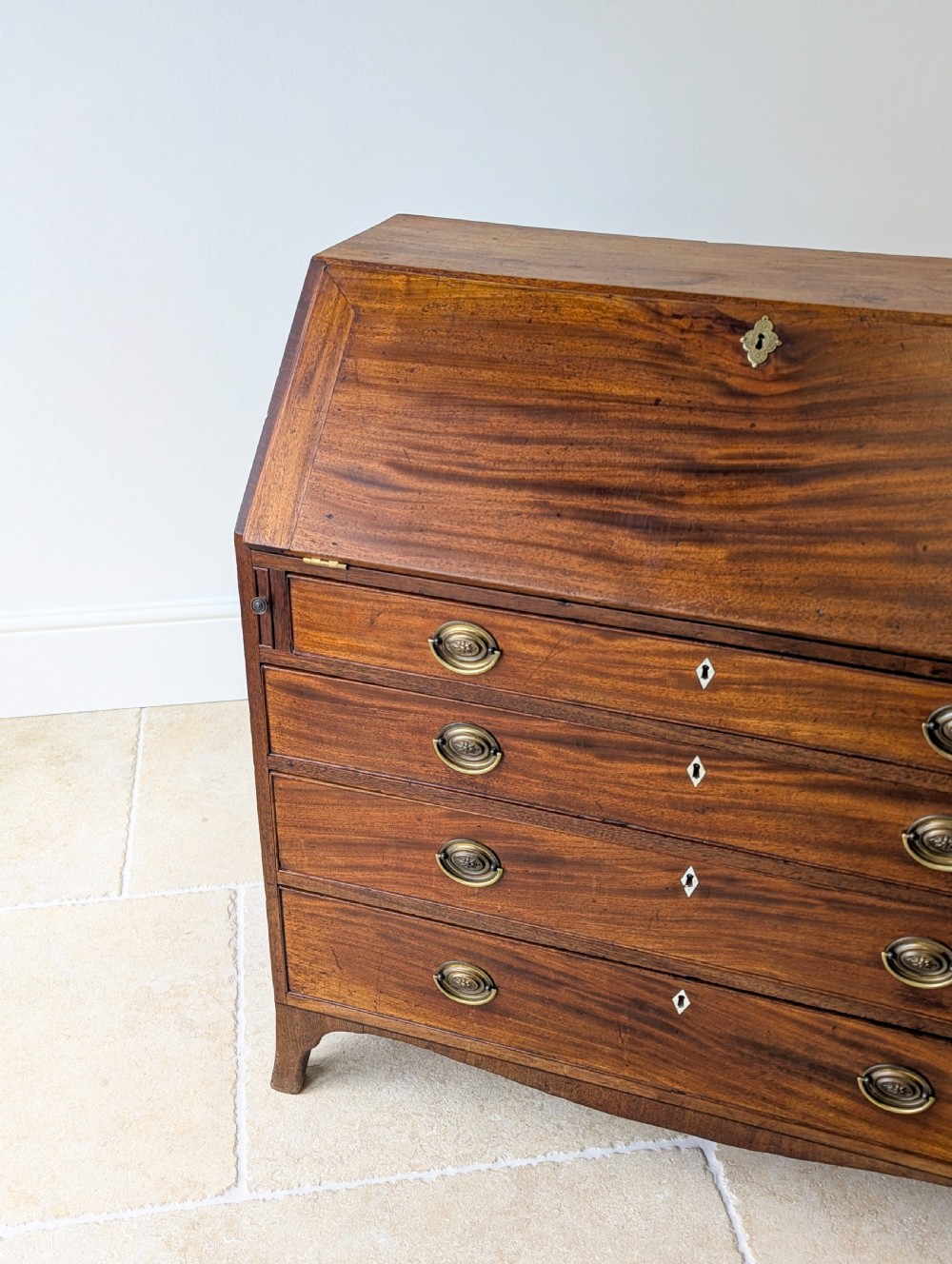 An antique Georgian mahogany slant-front bureau featuring four graduated long drawers with brass oval drop handles and shaped bracket feet. View X