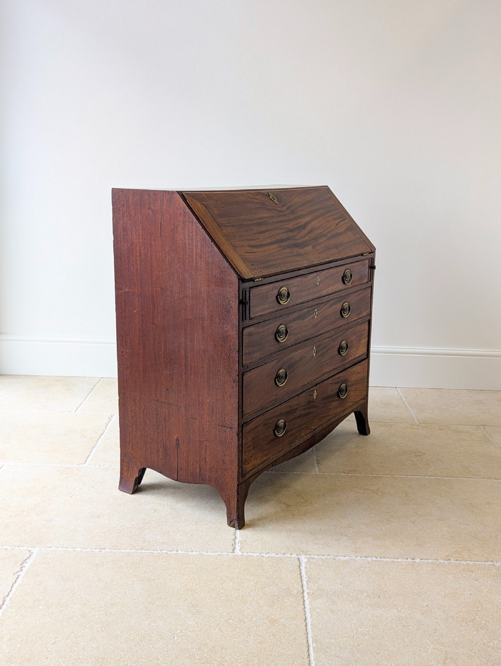 An antique Georgian mahogany slant-front bureau featuring four graduated long drawers with brass oval drop handles and shaped bracket feet. View XI