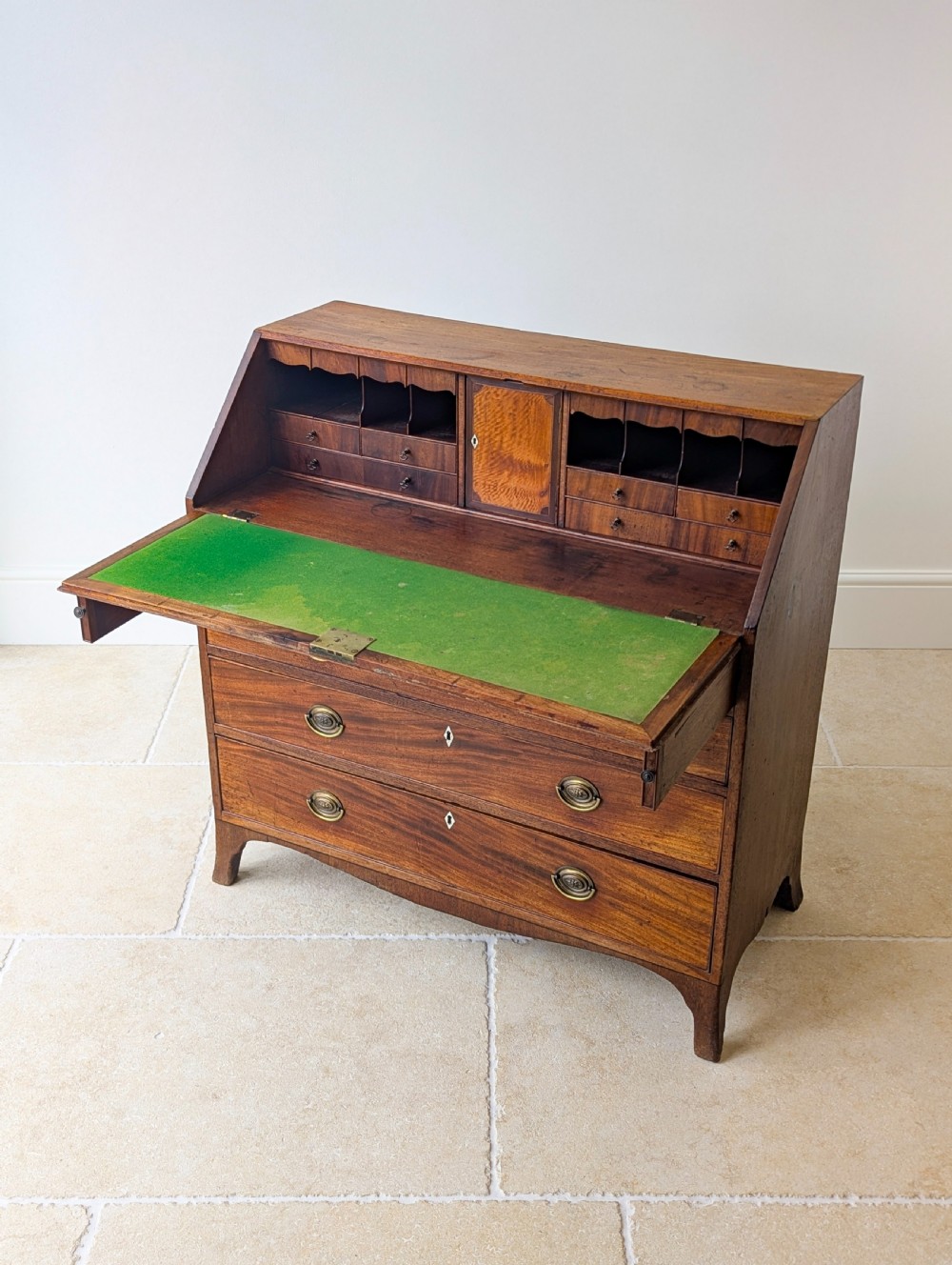 An antique Georgian mahogany slant-front bureau featuring four graduated long drawers with brass oval drop handles and shaped bracket feet. View XII