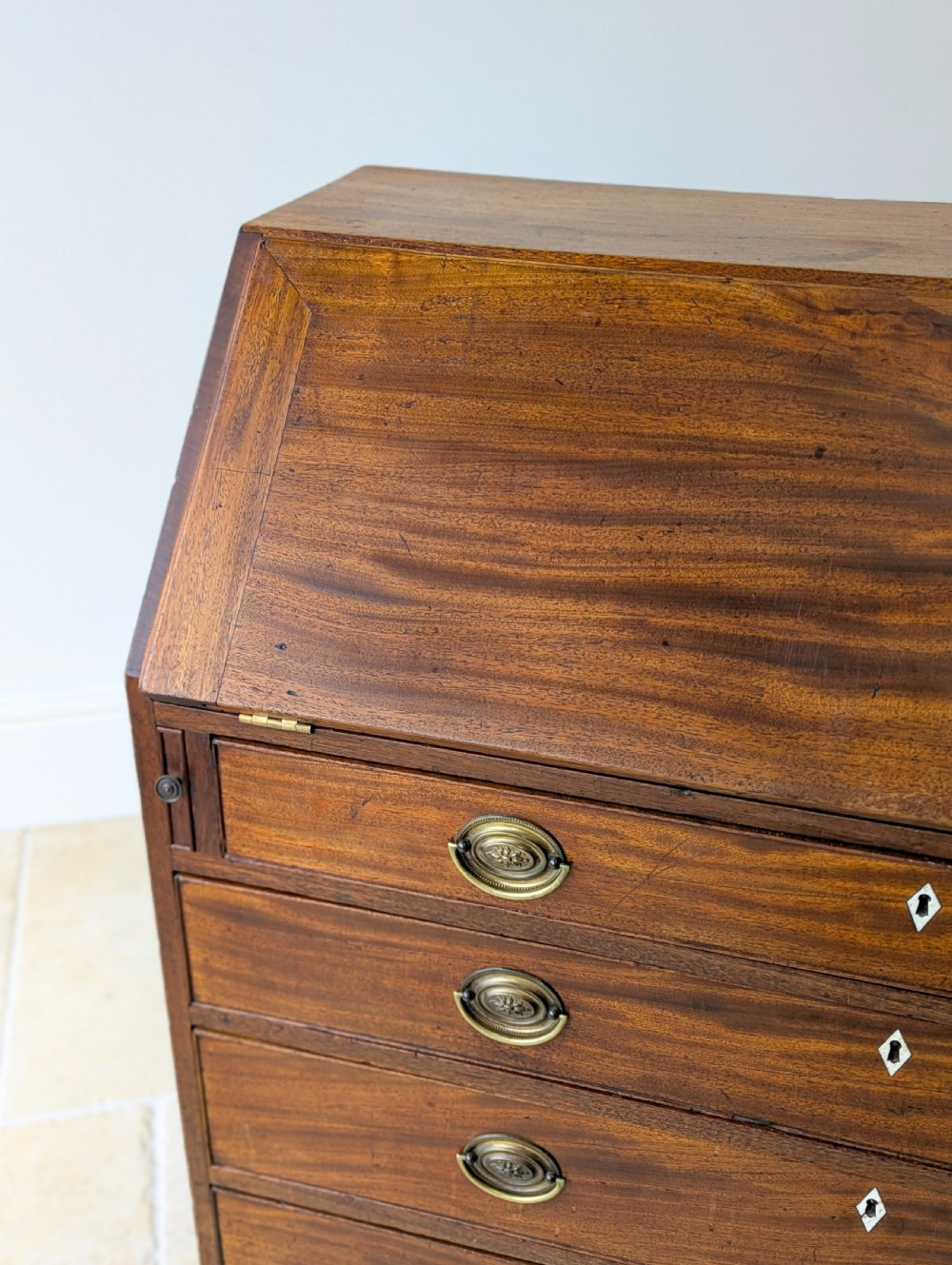 An antique Georgian mahogany slant-front bureau featuring four graduated long drawers with brass oval drop handles and shaped bracket feet. View XV