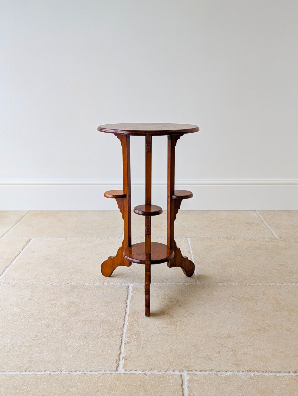 An early 20th-century stained beech occasional table featuring a circular top, three small side tiers, a lower circular shelf, and curved bracket feet. View V