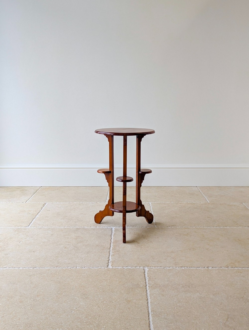 An early 20th-century stained beech occasional table featuring a circular top, three small side tiers, a lower circular shelf, and curved bracket feet. View XI