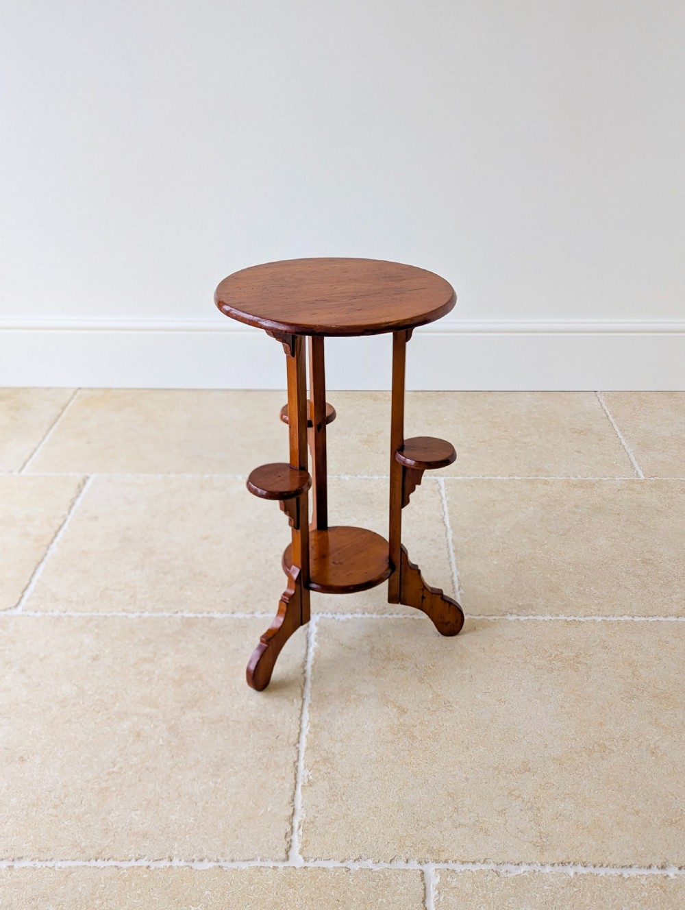 An early 20th-century stained beech occasional table featuring a circular top, three small side tiers, a lower circular shelf, and curved bracket feet. View XII