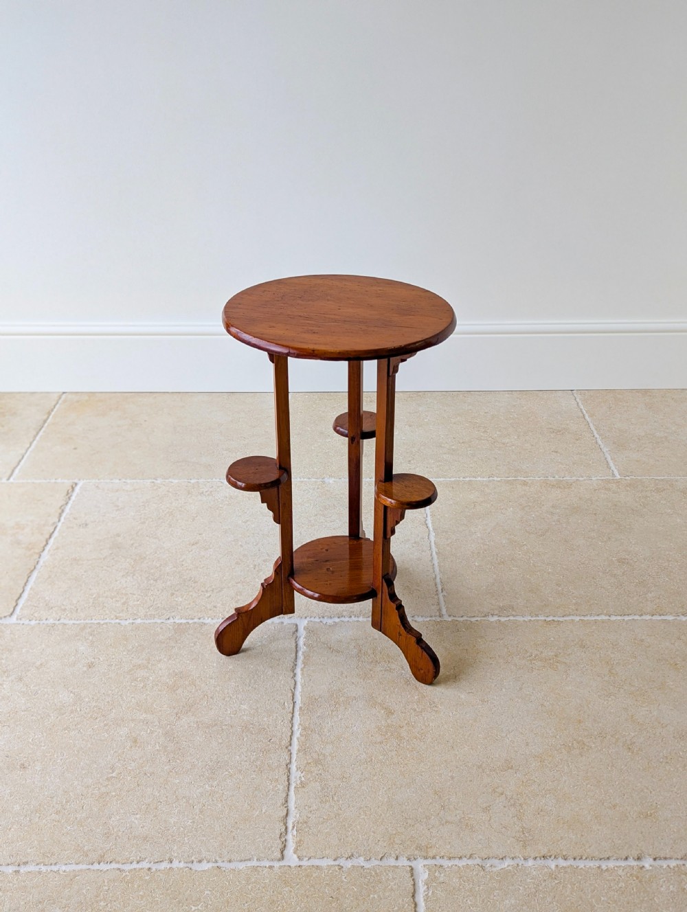 An early 20th-century stained beech occasional table featuring a circular top, three small side tiers, a lower circular shelf, and curved bracket feet. View XV