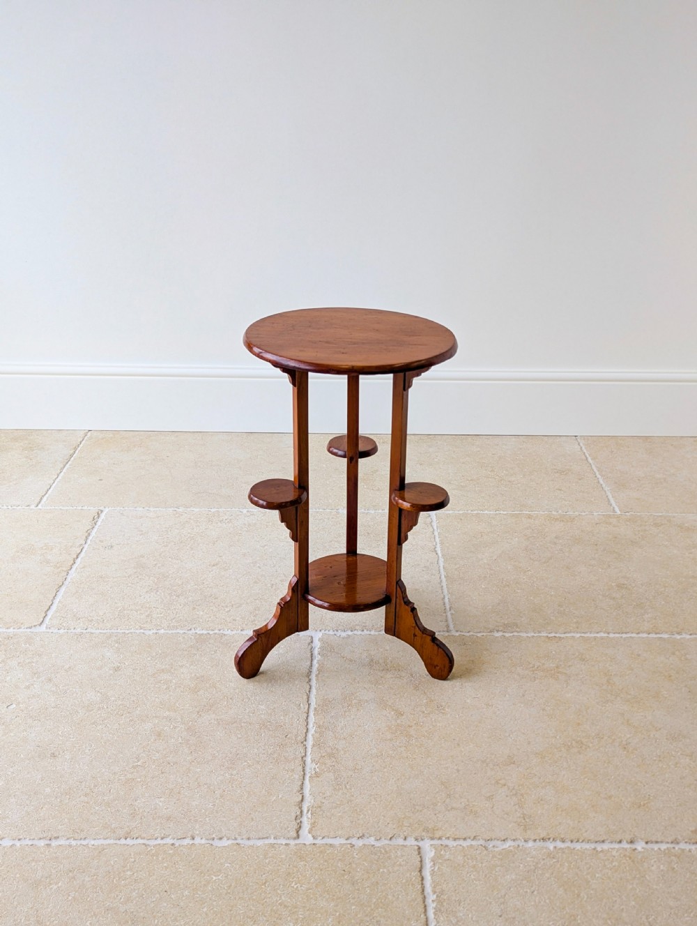 An early 20th-century stained beech occasional table featuring a circular top, three small side tiers, a lower circular shelf, and curved bracket feet. View XVIII