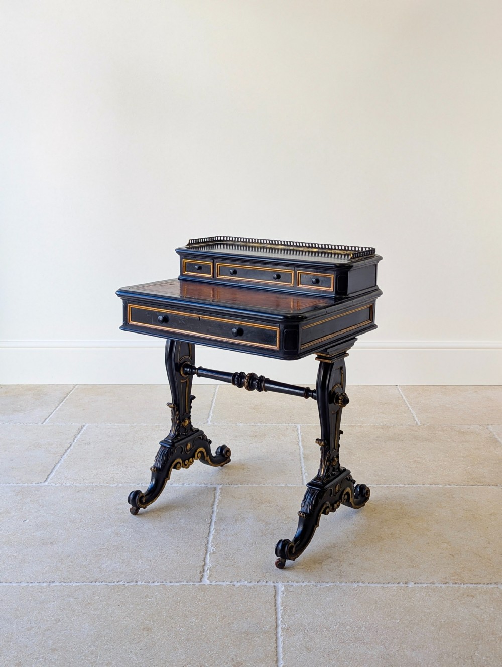 A Victorian ebonised bonheur du jour writing desk featuring gilded accents, a raised superstructure with small drawers, a brass gallery rail, and turned stretcher support.