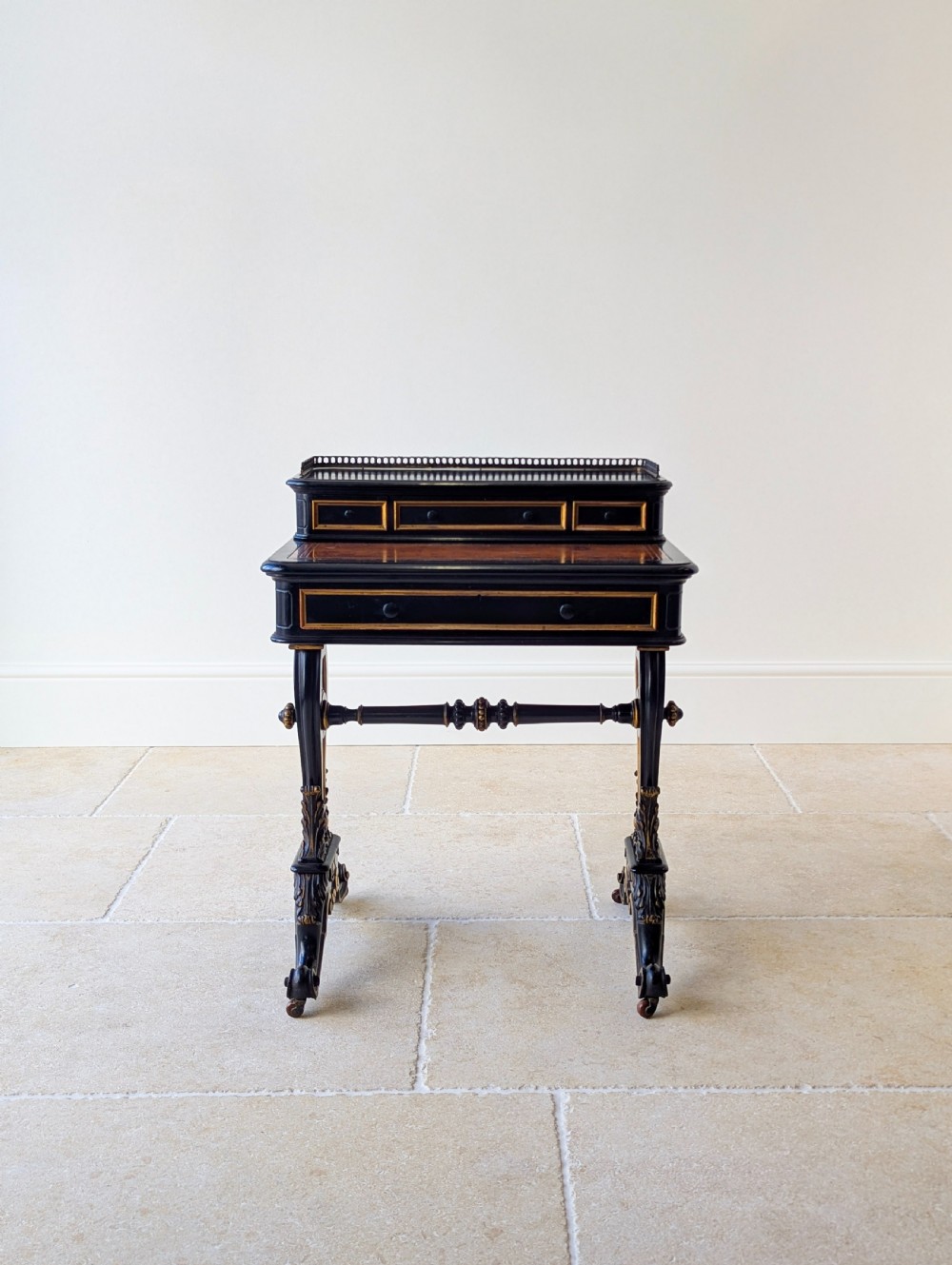 A Victorian ebonised bonheur du jour writing desk featuring gilded accents, a raised superstructure with small drawers, a brass gallery rail, and turned stretcher support. View II