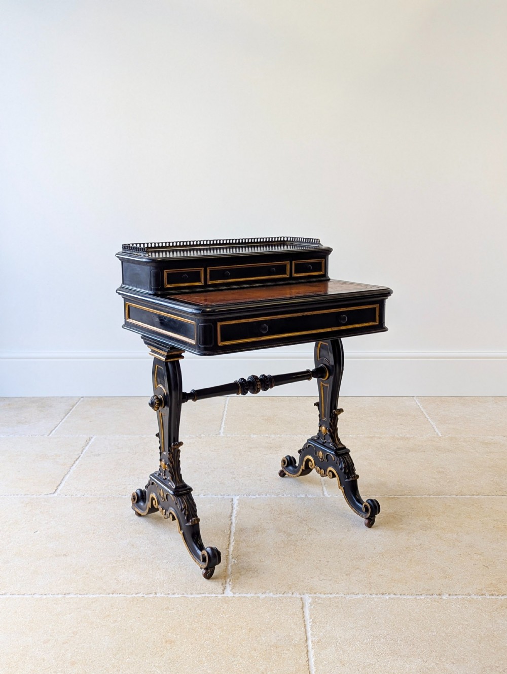 A Victorian ebonised bonheur du jour writing desk featuring gilded accents, a raised superstructure with small drawers, a brass gallery rail, and turned stretcher support. View IV