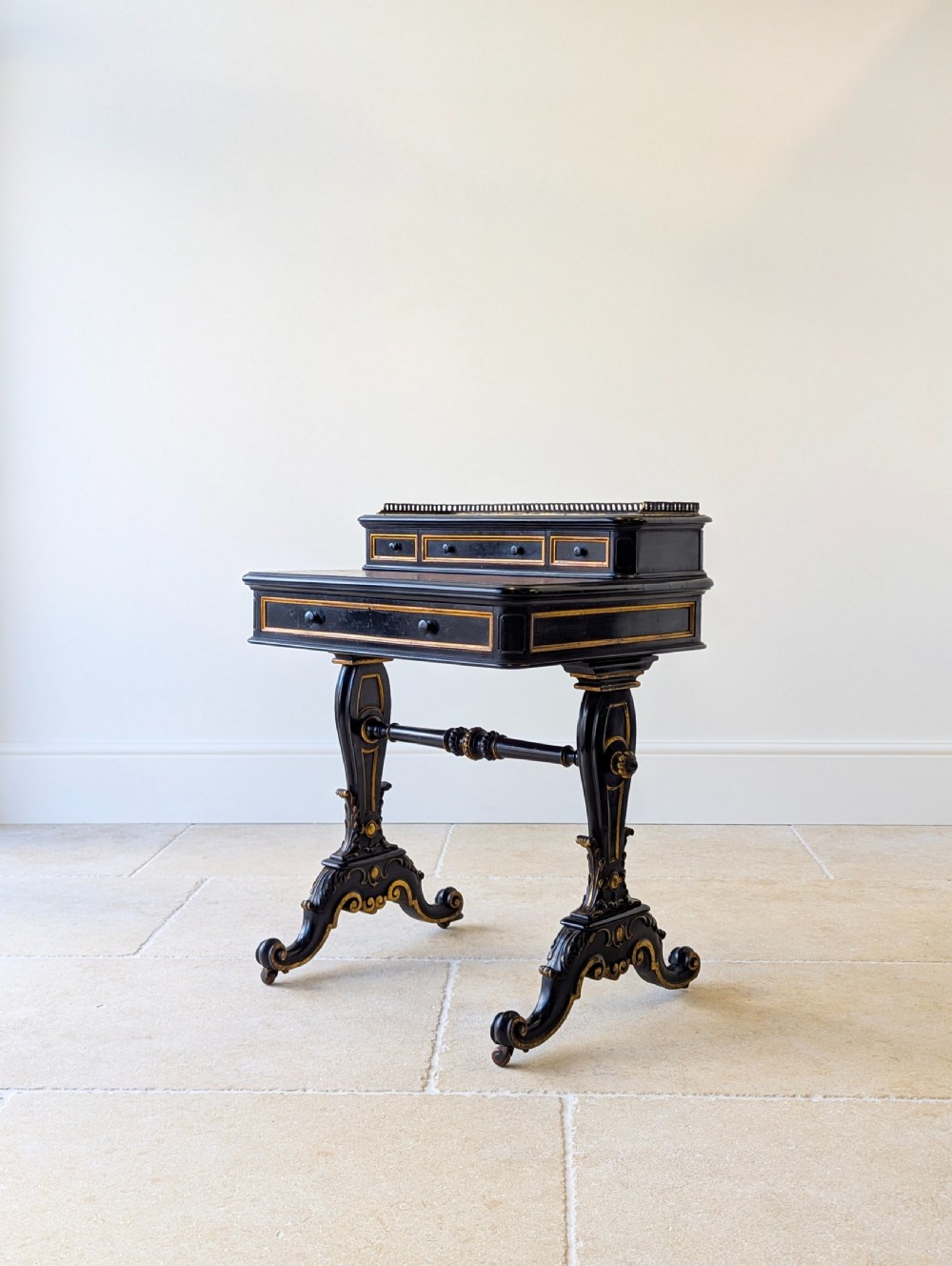 A Victorian ebonised bonheur du jour writing desk featuring gilded accents, a raised superstructure with small drawers, a brass gallery rail, and turned stretcher support. View VI