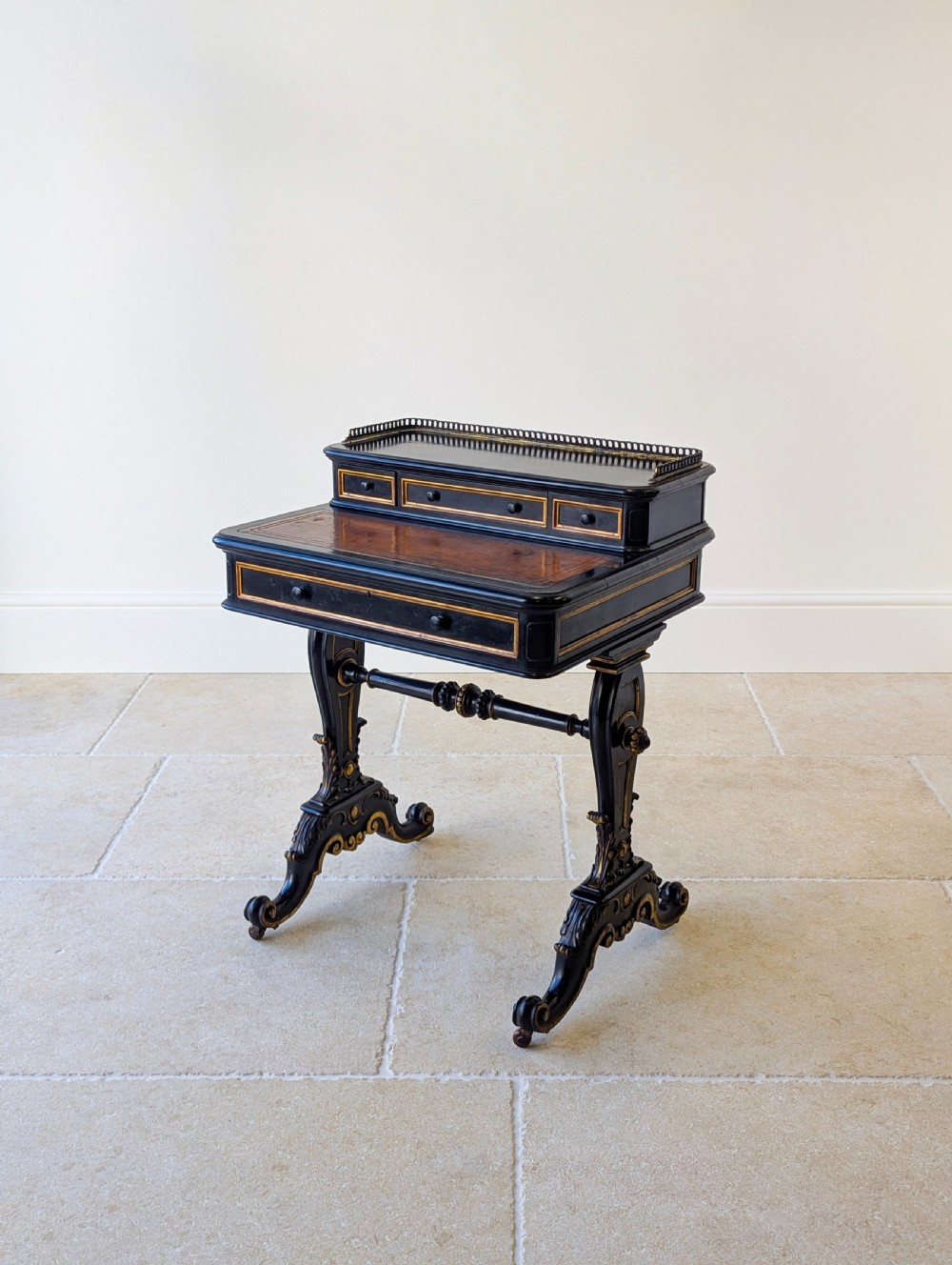A Victorian ebonised bonheur du jour writing desk featuring gilded accents, a raised superstructure with small drawers, a brass gallery rail, and turned stretcher support. View VIII