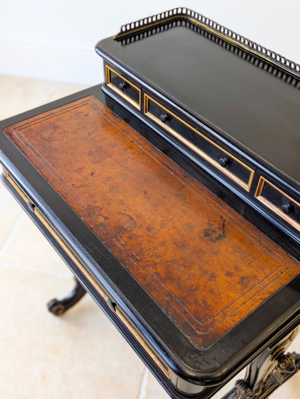 A Victorian ebonised bonheur du jour writing desk featuring gilded accents, a raised superstructure with small drawers, a brass gallery rail, and turned stretcher support. View IX