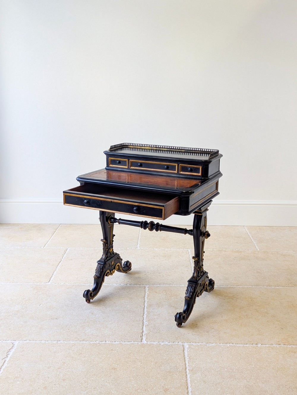 A Victorian ebonised bonheur du jour writing desk featuring gilded accents, a raised superstructure with small drawers, a brass gallery rail, and turned stretcher support. View XIV