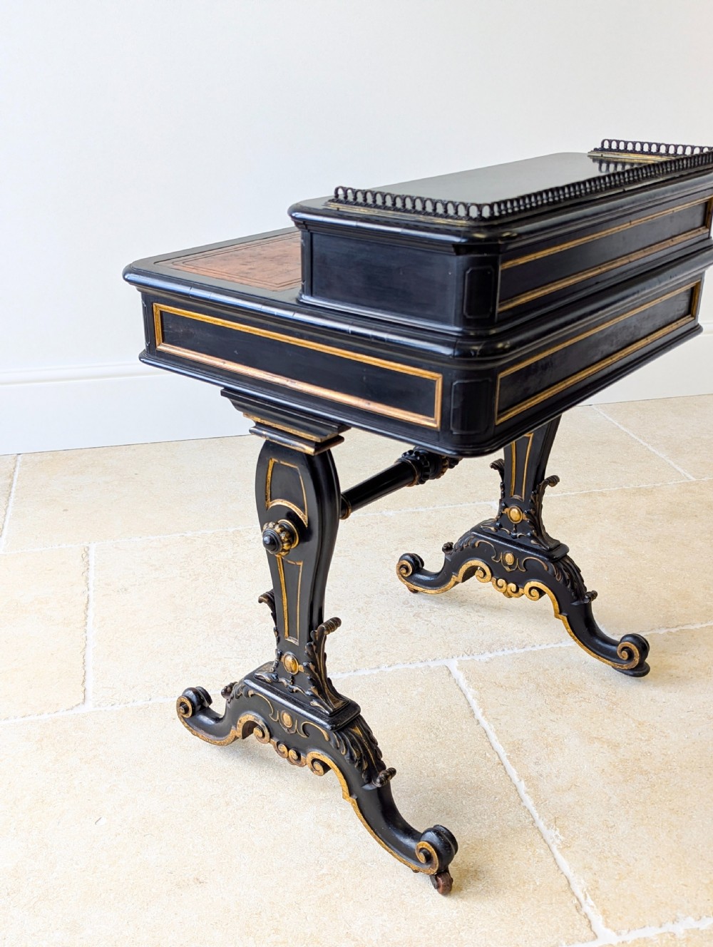 A Victorian ebonised bonheur du jour writing desk featuring gilded accents, a raised superstructure with small drawers, a brass gallery rail, and turned stretcher support. View XV