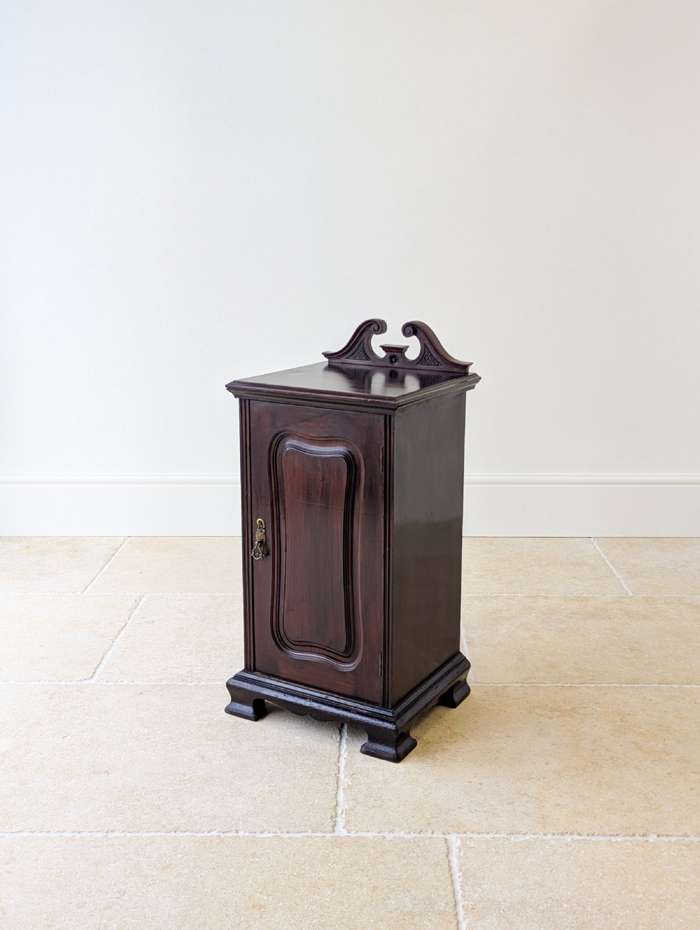 An antique Victorian dark mahogany bedside cabinet with a carved gallery back, a single door with a molded panel, and a sturdy plinth base.