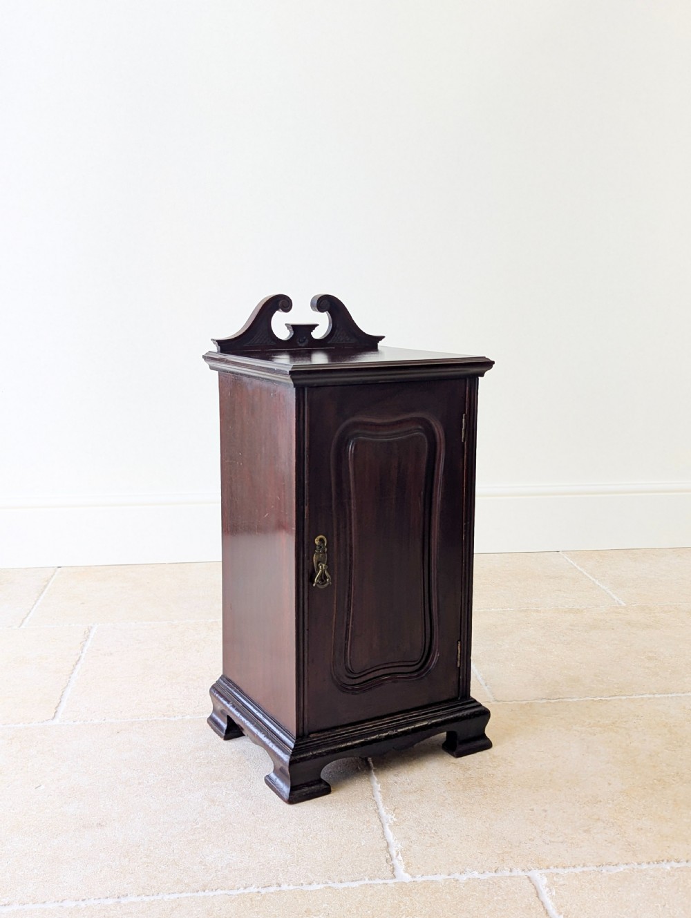 An antique Victorian dark mahogany bedside cabinet with a carved gallery back, a single door with a molded panel, and a sturdy plinth base. View VI