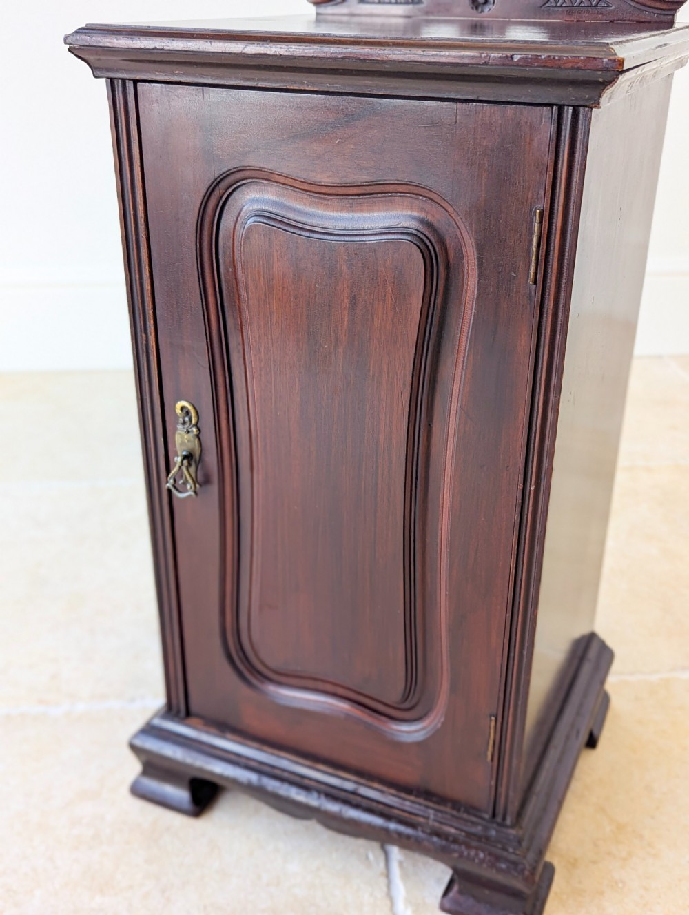 An antique Victorian dark mahogany bedside cabinet with a carved gallery back, a single door with a molded panel, and a sturdy plinth base. View IX