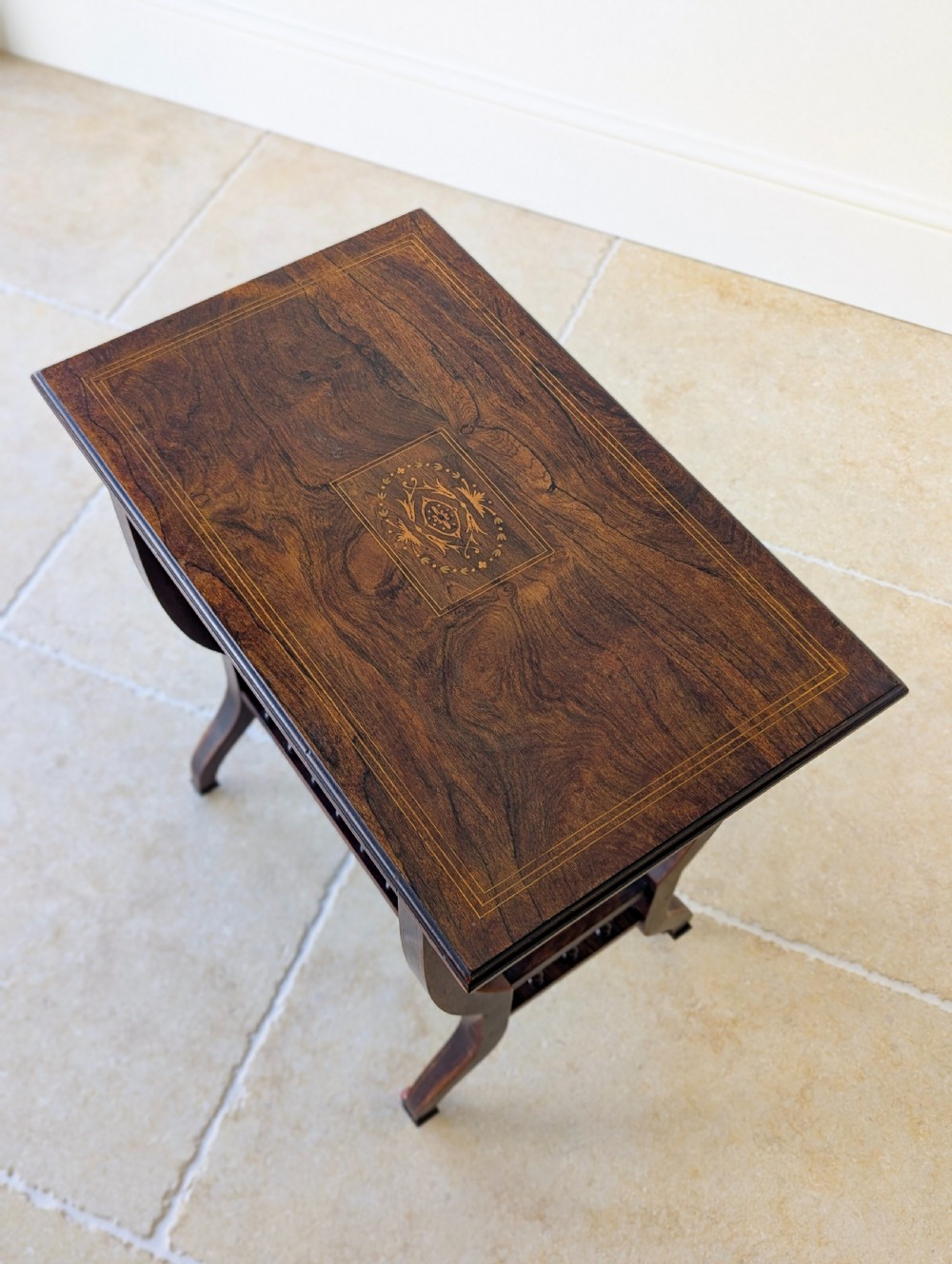An antique Edwardian dark rosewood occasional table featuring out-swept legs, brass castors, a decorative shaped apron, and a lower shelf enclosed by turned vertical spindles. View II
