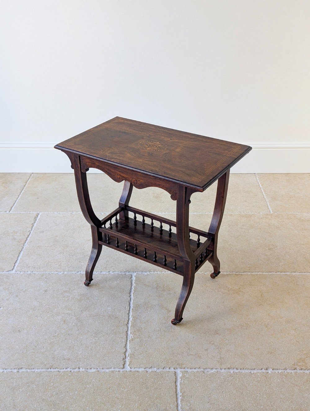 An antique Edwardian dark rosewood occasional table featuring out-swept legs, brass castors, a decorative shaped apron, and a lower shelf enclosed by turned vertical spindles. View III