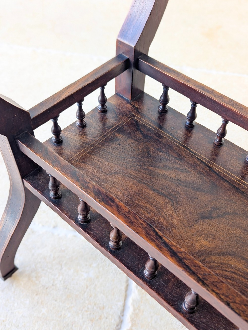 An antique Edwardian dark rosewood occasional table featuring out-swept legs, brass castors, a decorative shaped apron, and a lower shelf enclosed by turned vertical spindles. View IV