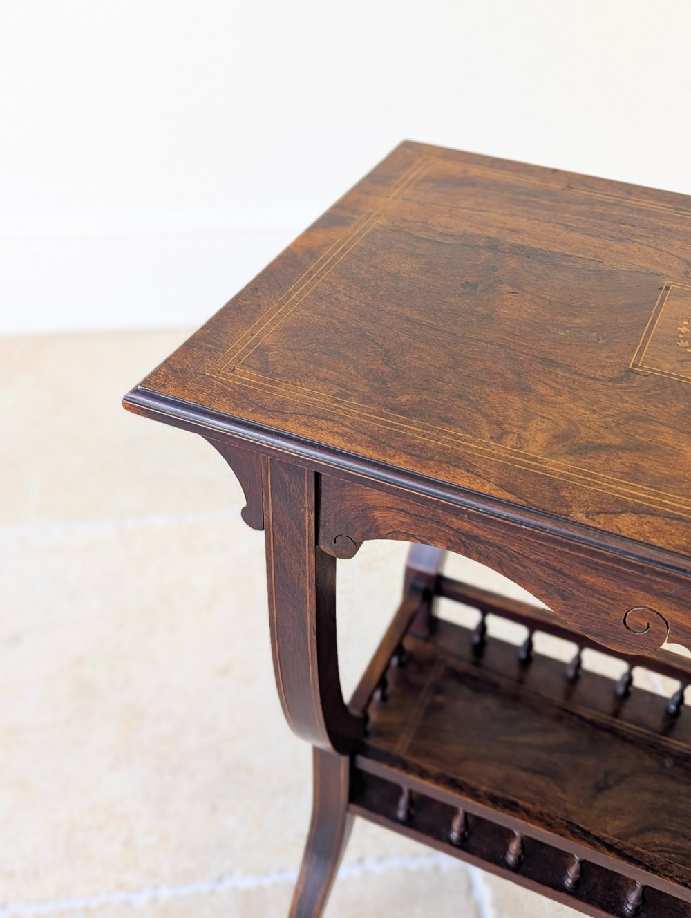 An antique Edwardian dark rosewood occasional table featuring out-swept legs, brass castors, a decorative shaped apron, and a lower shelf enclosed by turned vertical spindles. View VI