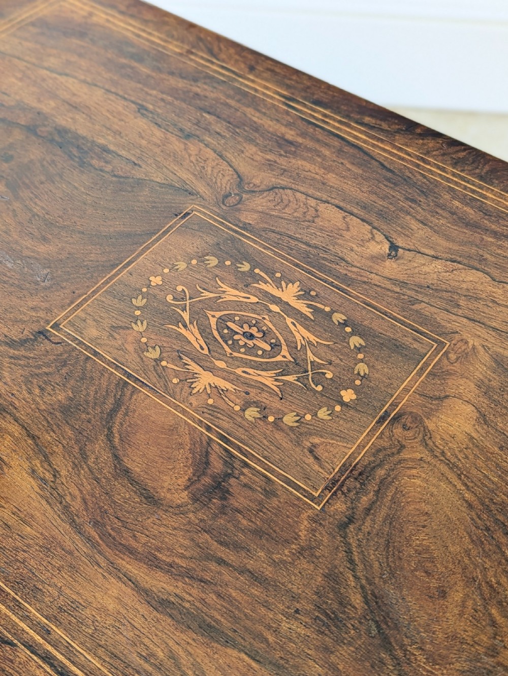 An antique Edwardian dark rosewood occasional table featuring out-swept legs, brass castors, a decorative shaped apron, and a lower shelf enclosed by turned vertical spindles. View VIII