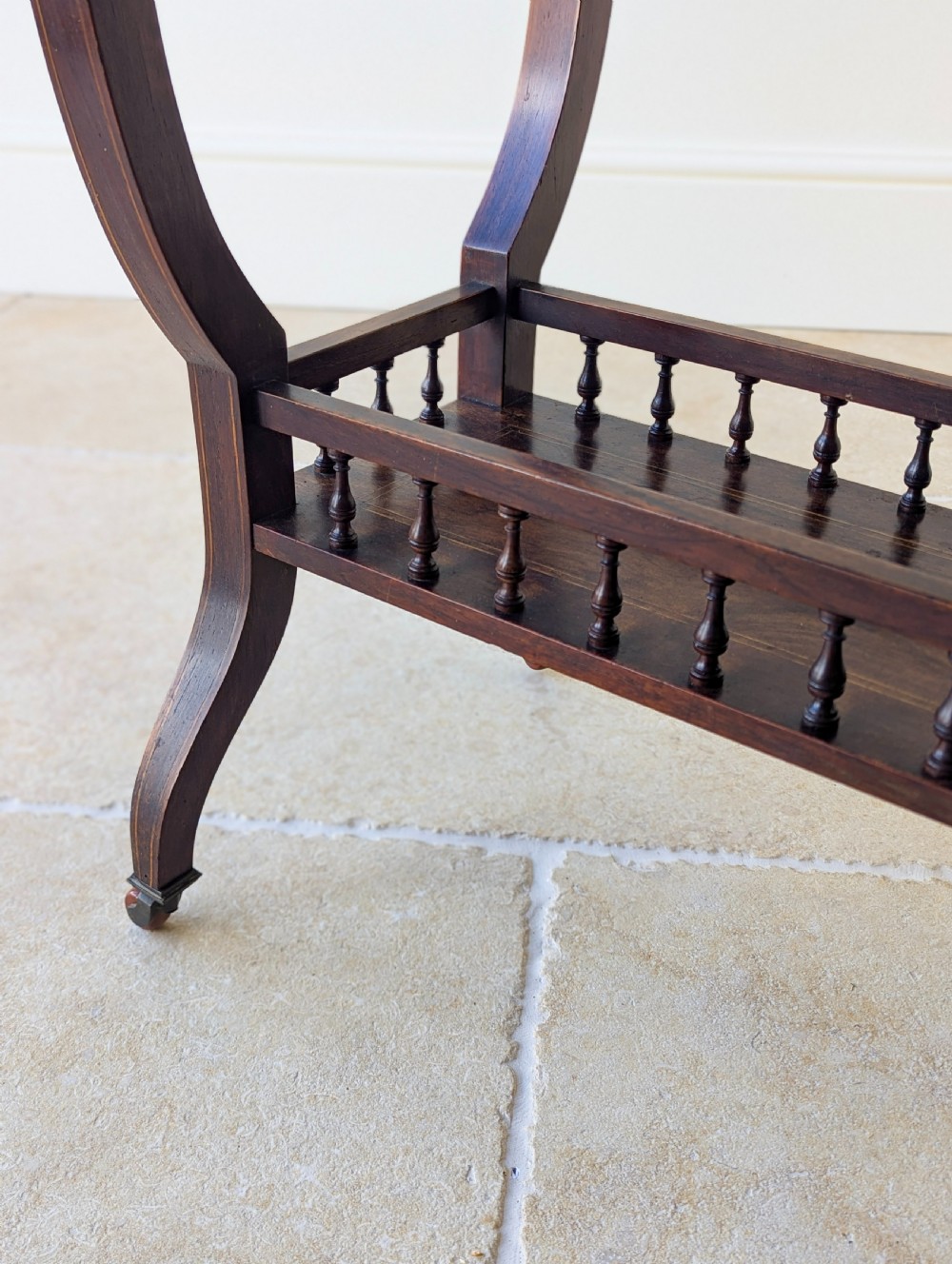 An antique Edwardian dark rosewood occasional table featuring out-swept legs, brass castors, a decorative shaped apron, and a lower shelf enclosed by turned vertical spindles. View IX