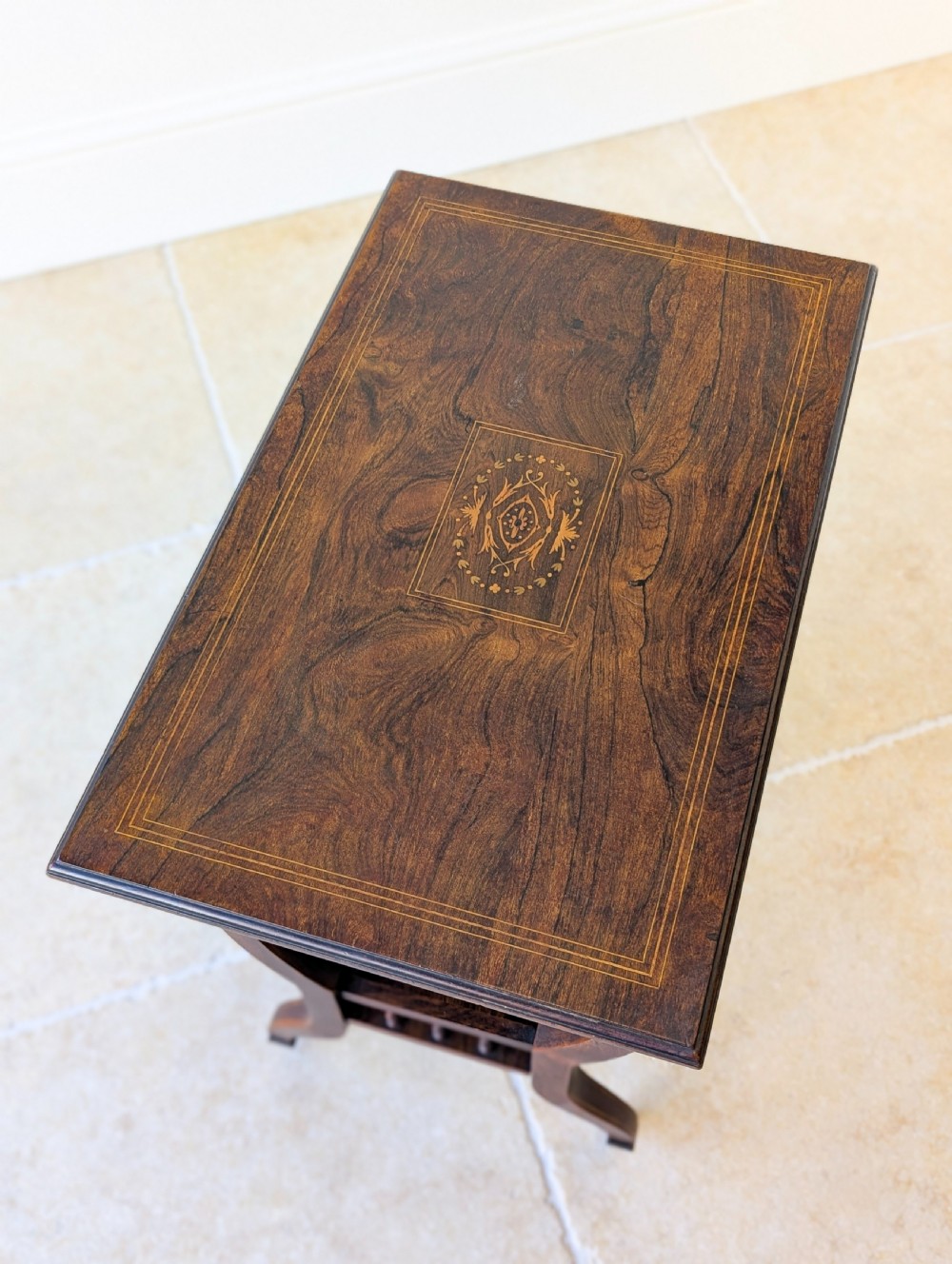 An antique Edwardian dark rosewood occasional table featuring out-swept legs, brass castors, a decorative shaped apron, and a lower shelf enclosed by turned vertical spindles. View XIII