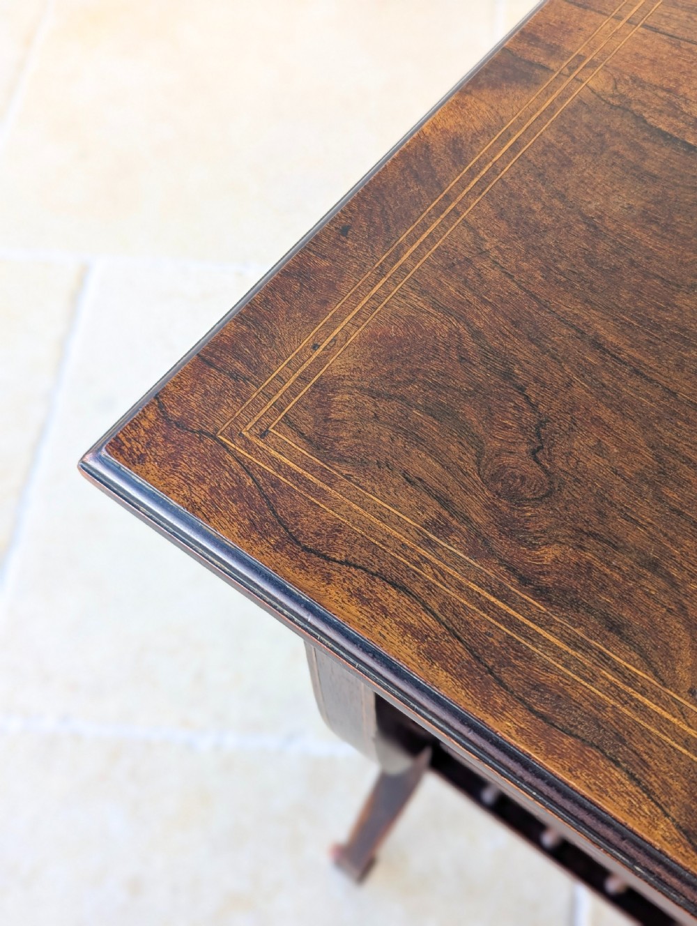An antique Edwardian dark rosewood occasional table featuring out-swept legs, brass castors, a decorative shaped apron, and a lower shelf enclosed by turned vertical spindles. View XV