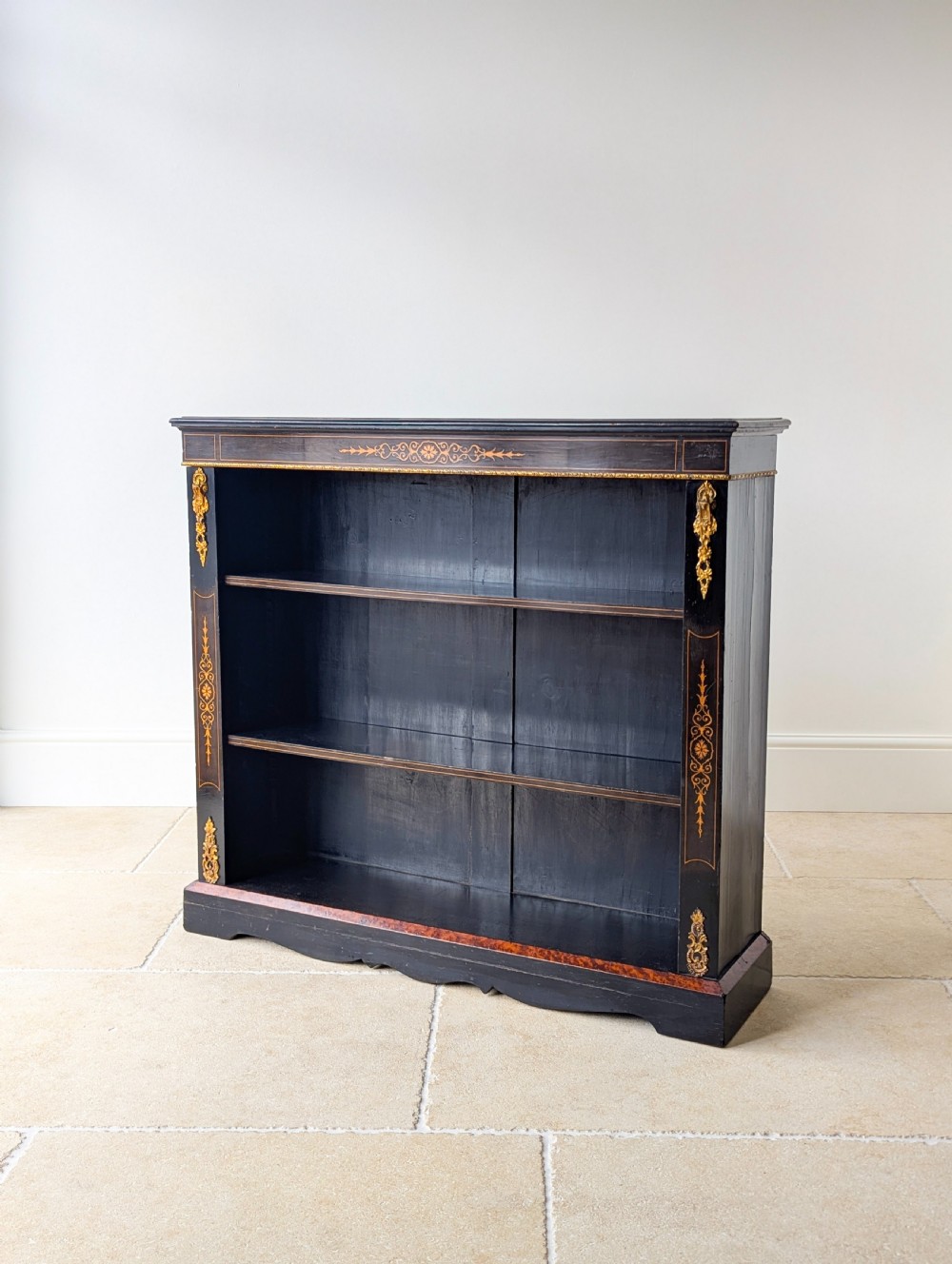 A Victorian ebonised open bookcase with three shelves, gold inlay, and gilt bronze mounts along the side uprights.