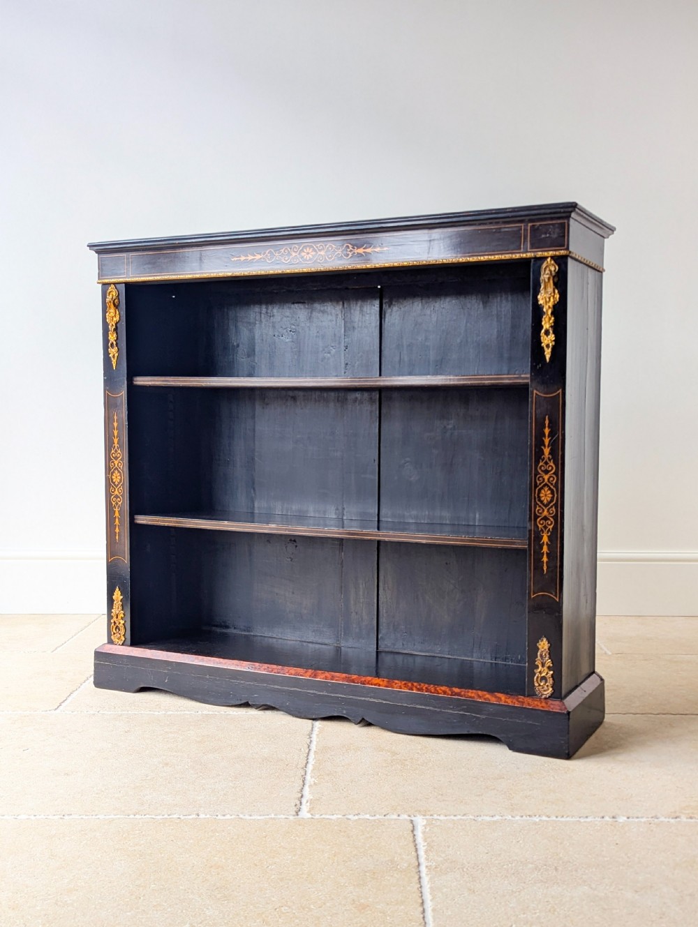 A Victorian ebonised open bookcase with three shelves, gold inlay, and gilt bronze mounts along the side uprights. View V
