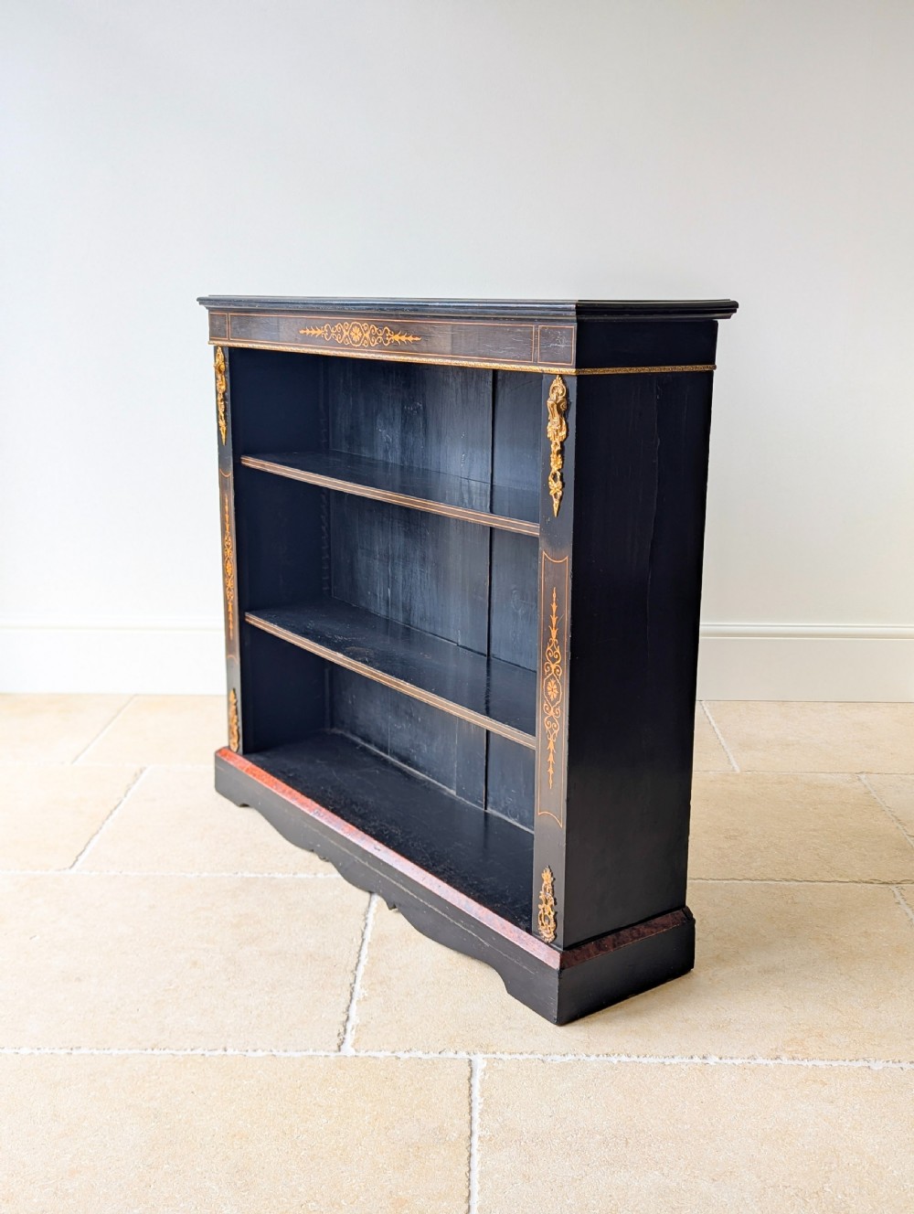 A Victorian ebonised open bookcase with three shelves, gold inlay, and gilt bronze mounts along the side uprights. View VII