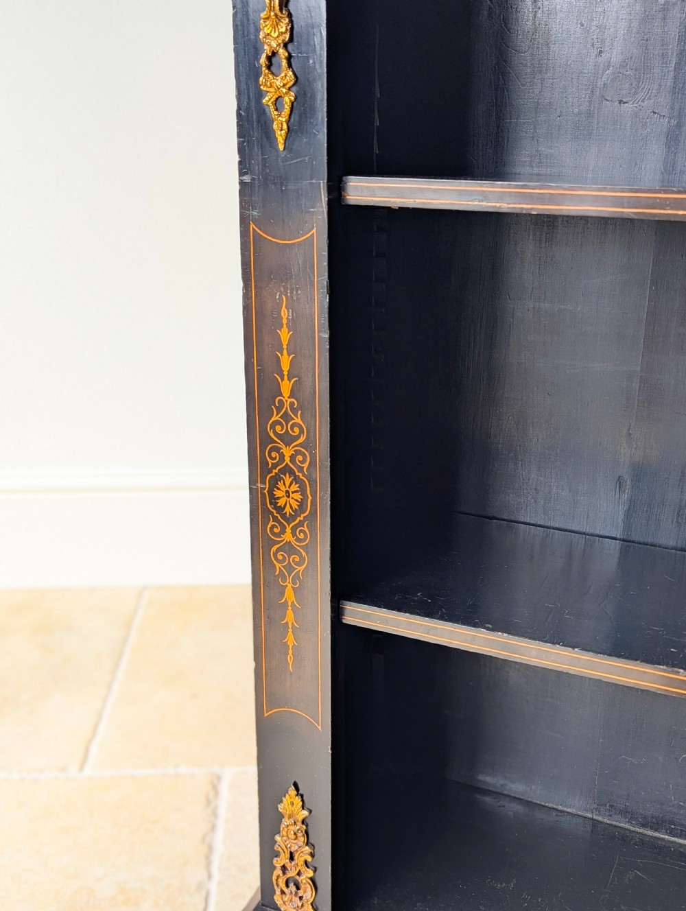 A Victorian ebonised open bookcase with three shelves, gold inlay, and gilt bronze mounts along the side uprights. View IX