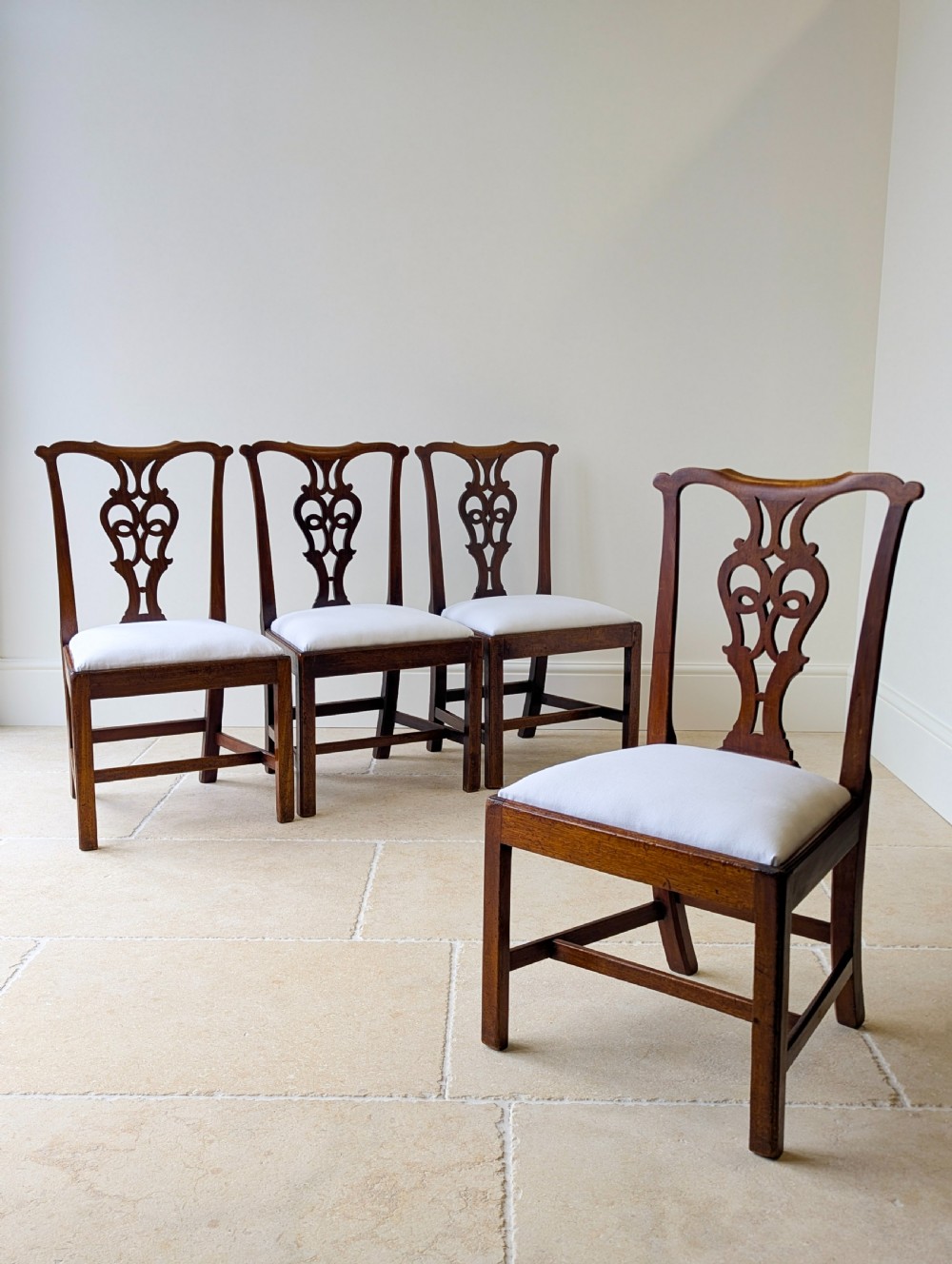 A set of four antique Georgian Chippendale mahogany dining chairs with pierced splat backs, drop-in white fabric seats, and H-stretcher bases.