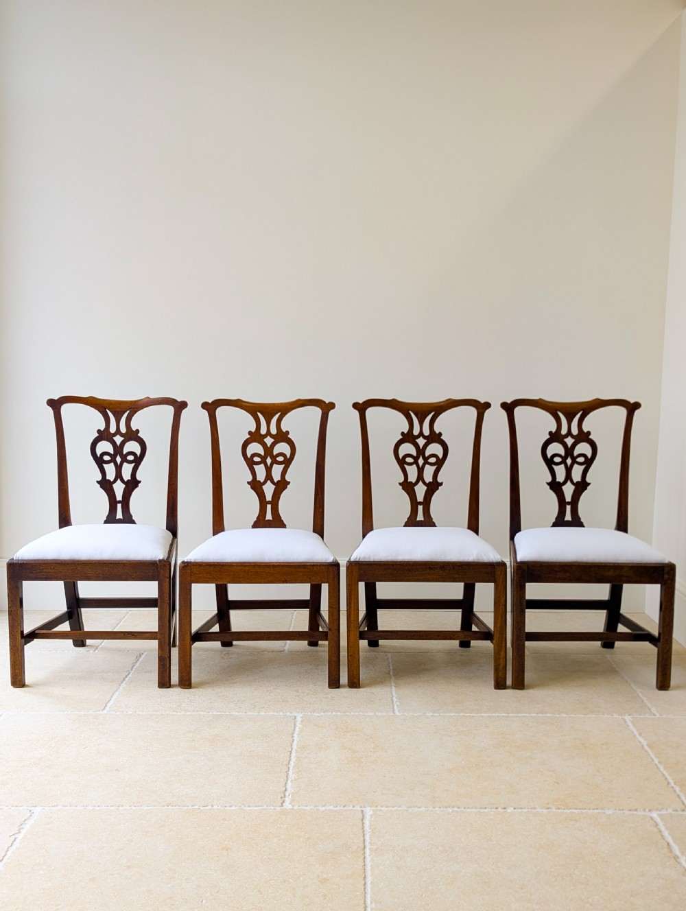 A set of four antique Georgian Chippendale mahogany dining chairs with pierced splat backs, drop-in white fabric seats, and H-stretcher bases. View II