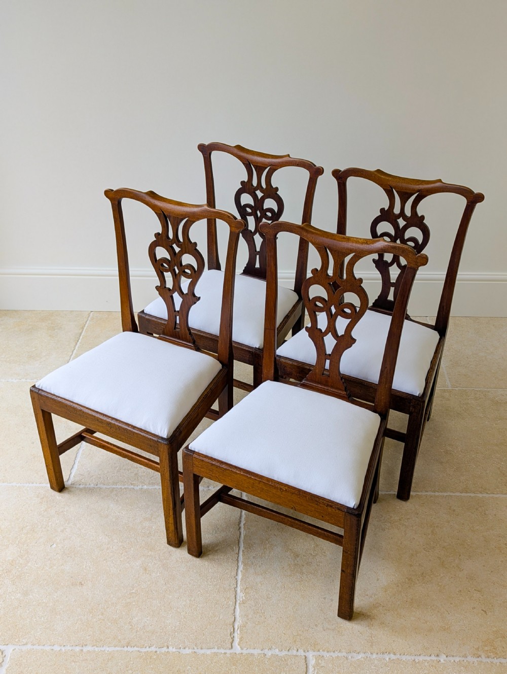A set of four antique Georgian Chippendale mahogany dining chairs with pierced splat backs, drop-in white fabric seats, and H-stretcher bases. View IV