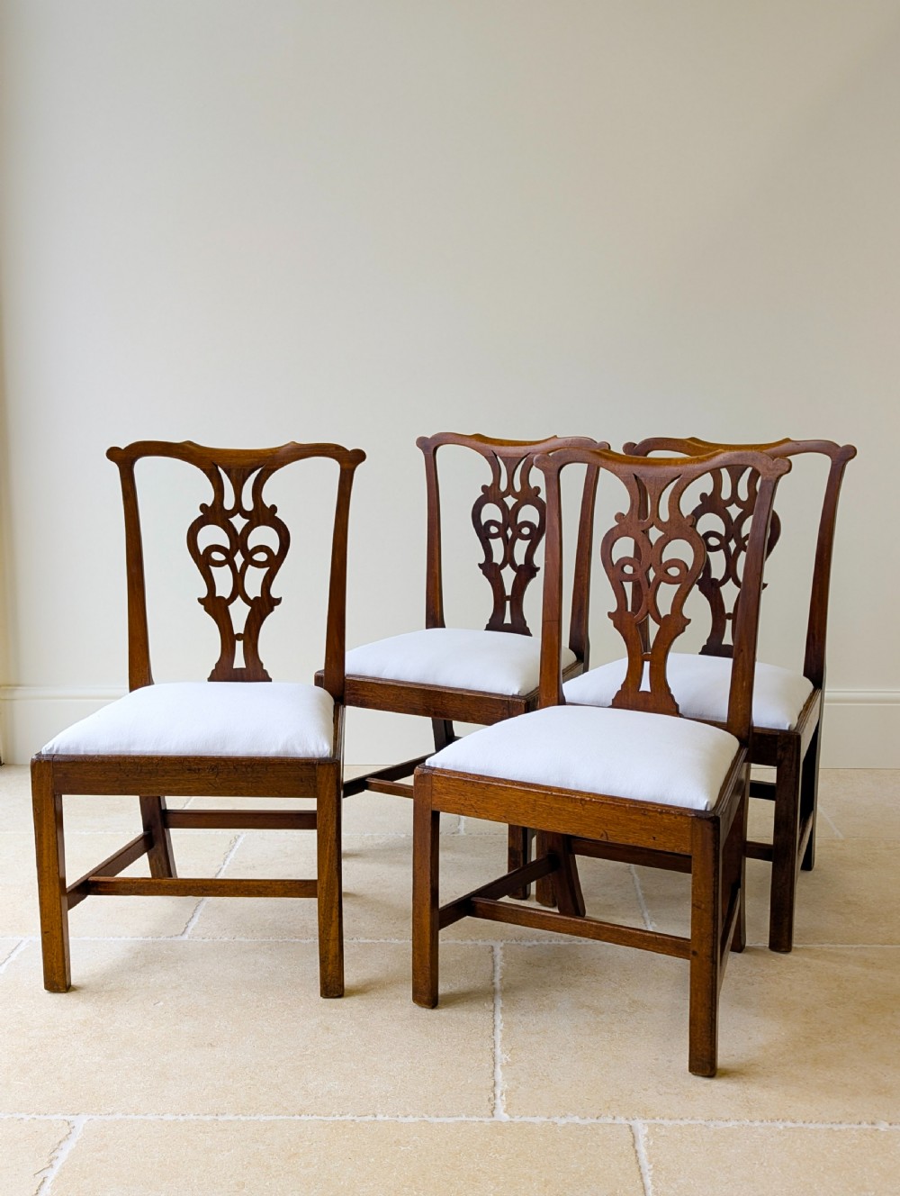 A set of four antique Georgian Chippendale mahogany dining chairs with pierced splat backs, drop-in white fabric seats, and H-stretcher bases. View V