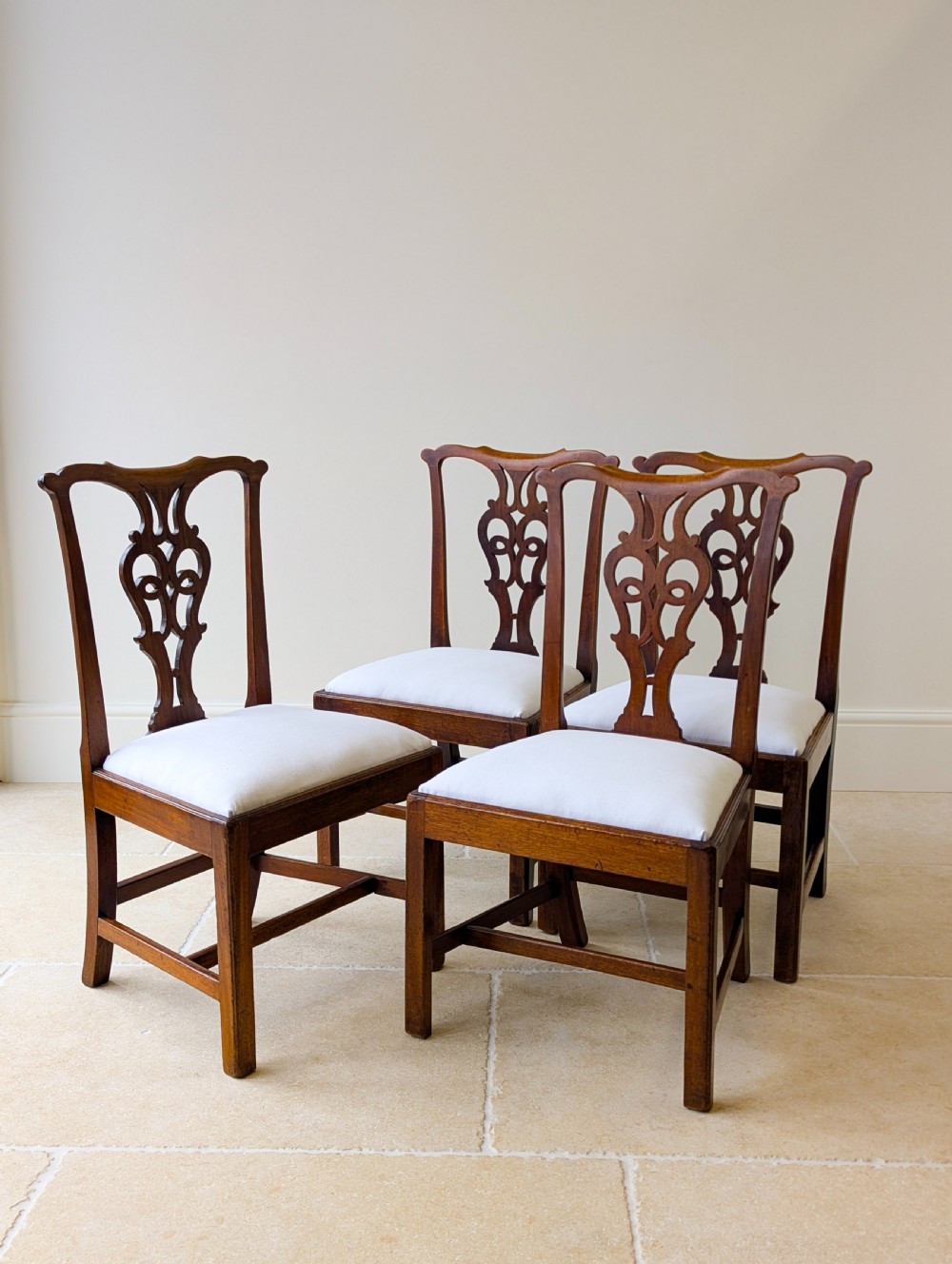 A set of four antique Georgian Chippendale mahogany dining chairs with pierced splat backs, drop-in white fabric seats, and H-stretcher bases. View VI