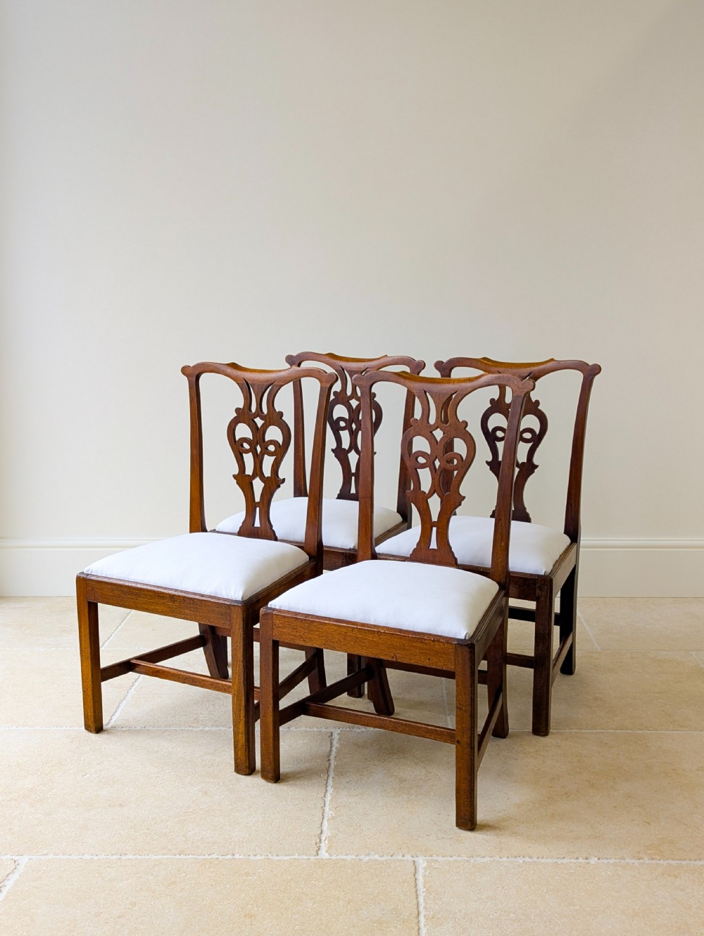 A set of four antique Georgian Chippendale mahogany dining chairs with pierced splat backs, drop-in white fabric seats, and H-stretcher bases. View VII