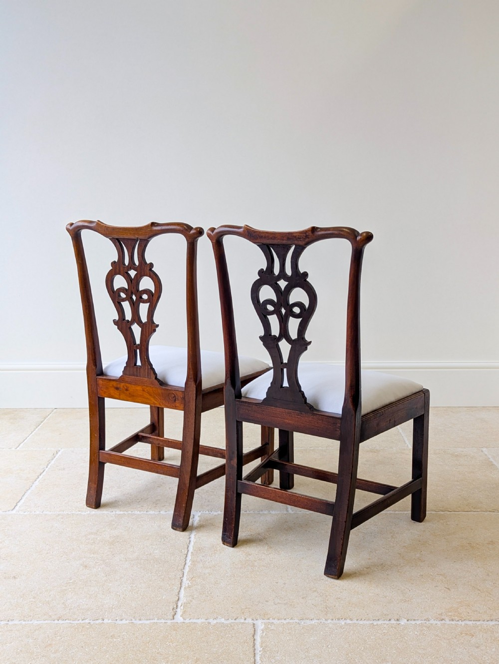 A set of four antique Georgian Chippendale mahogany dining chairs with pierced splat backs, drop-in white fabric seats, and H-stretcher bases. View IX