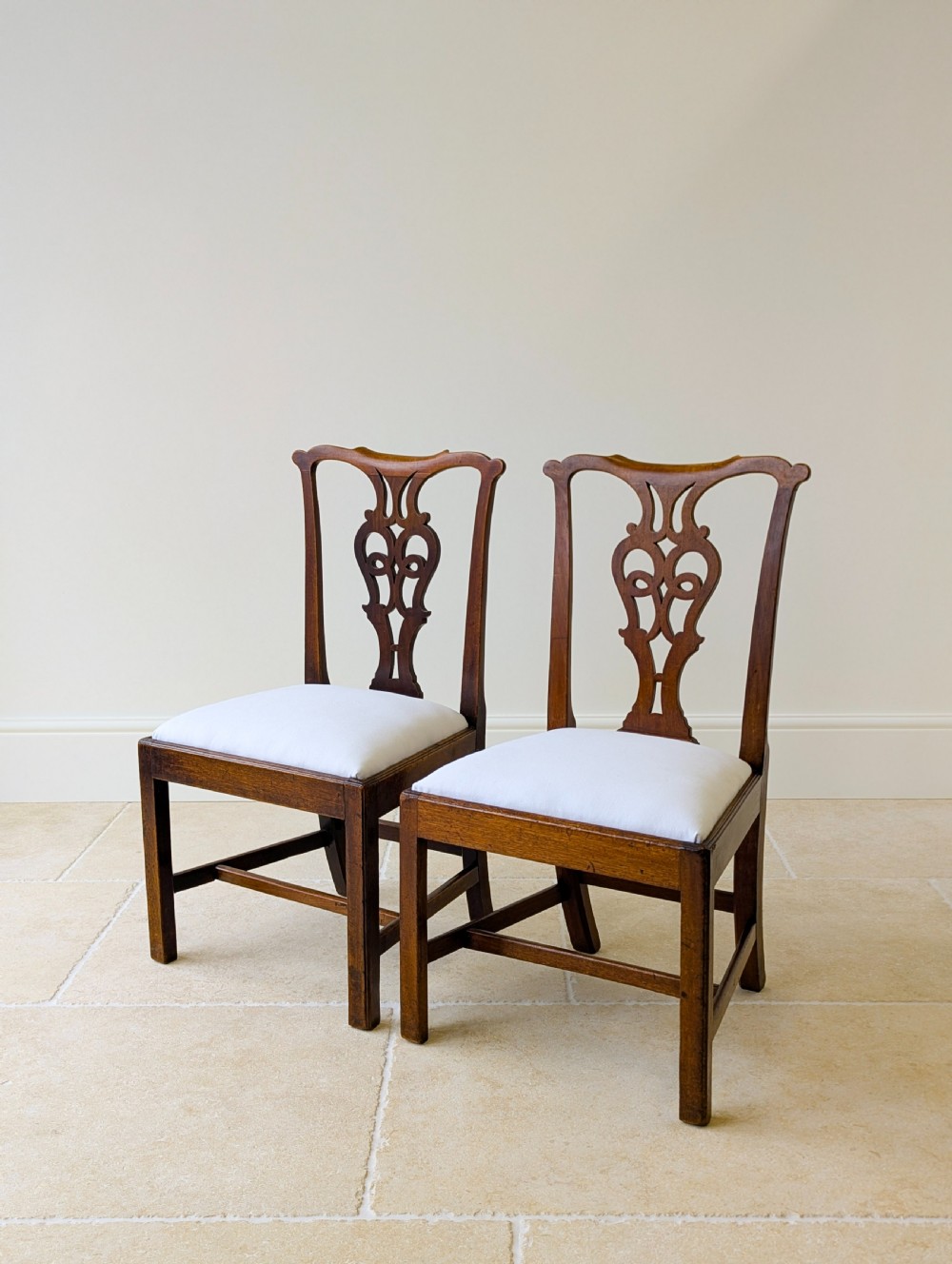 A set of four antique Georgian Chippendale mahogany dining chairs with pierced splat backs, drop-in white fabric seats, and H-stretcher bases. View X