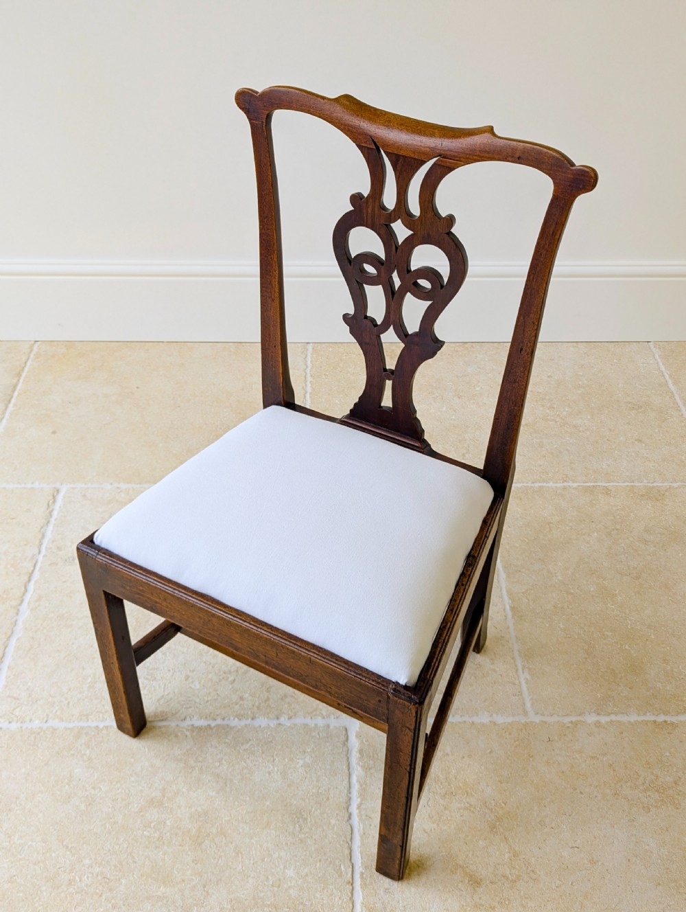 A set of four antique Georgian Chippendale mahogany dining chairs with pierced splat backs, drop-in white fabric seats, and H-stretcher bases. View XII