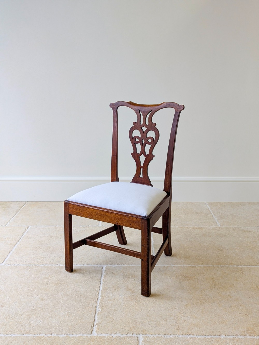 A set of four antique Georgian Chippendale mahogany dining chairs with pierced splat backs, drop-in white fabric seats, and H-stretcher bases. View XVI
