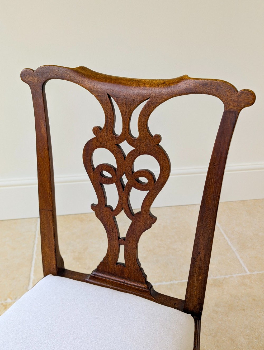 A set of four antique Georgian Chippendale mahogany dining chairs with pierced splat backs, drop-in white fabric seats, and H-stretcher bases. View XVII