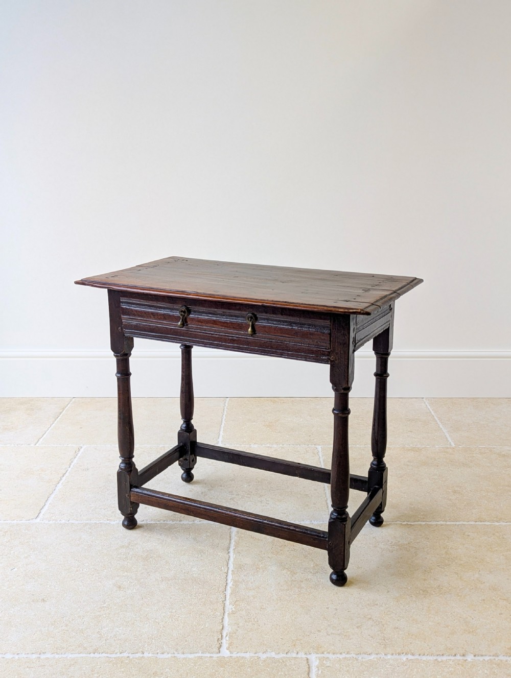A late 17th-century dark oak side table with turned legs, lower stretchers, and a single drawer featuring brass drop handles.