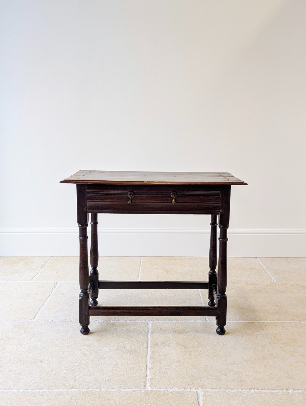A late 17th-century dark oak side table with turned legs, lower stretchers, and a single drawer featuring brass drop handles. View II